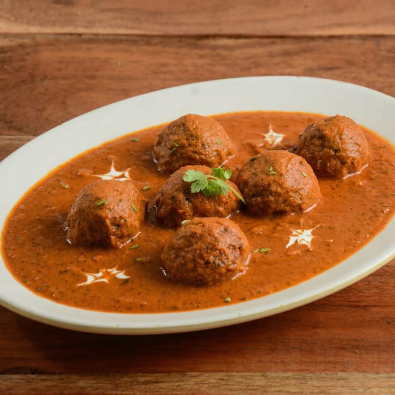 Malai Kofta, a popular Indian dish, served in a rich, creamy orange gravy on a white platter.