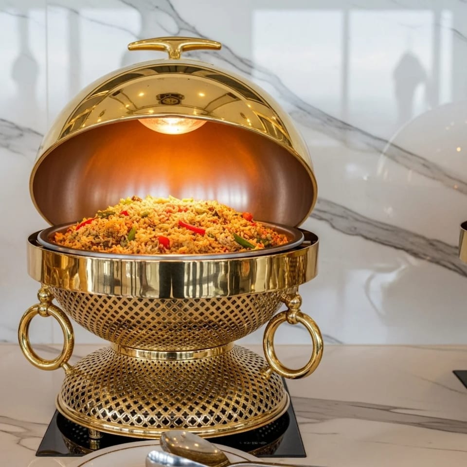 Golden chafing dish filled with colorful rice, illuminated by an internal light, on a marble counter.